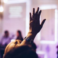 A person's hand is raised to ask a question at a speaking event 