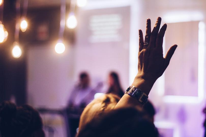 A person's hand is raised to ask a question at a speaking event 