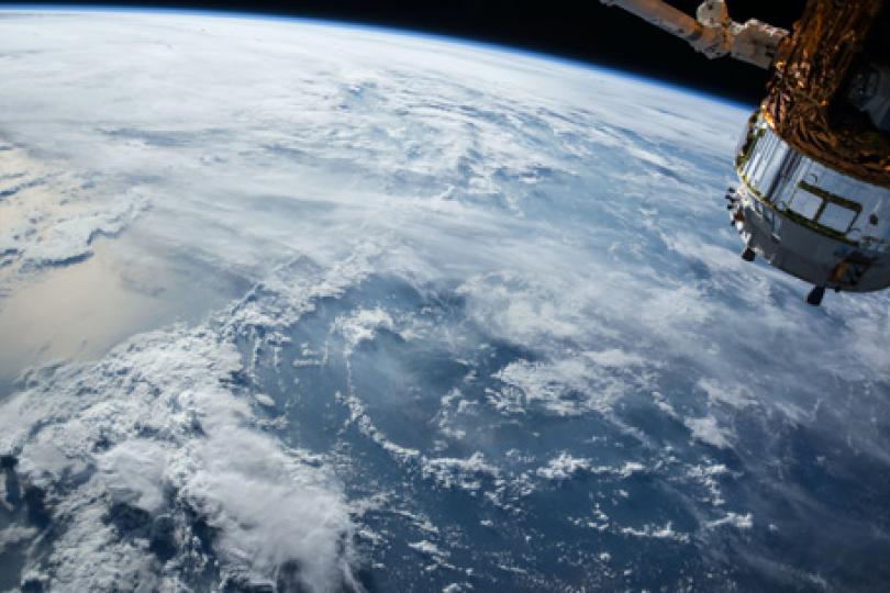 Picture of clouds over the ocean from space with a close-up of a satellite in the upper right corner.