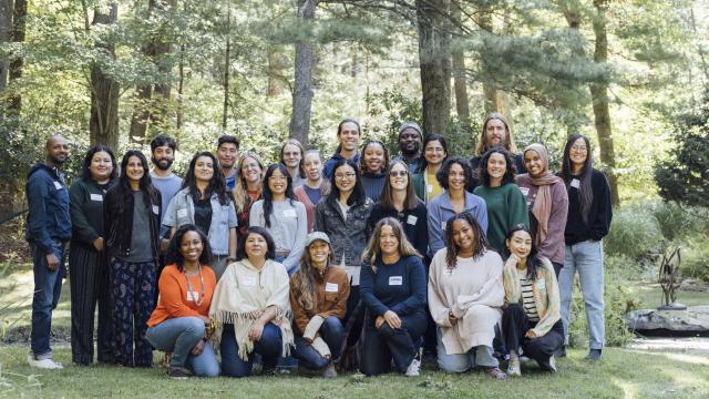 A group photo of fellows and staff smiling against a forest background, taken at the 2025 Switzer Fellows fall retreat. 