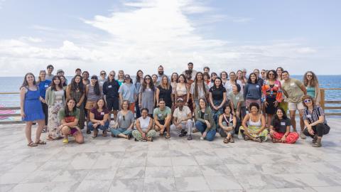 A group photo of the participants of the Fellowship to Friendship Switzer Network Celebration on a tile patio overlooking the ocean with white clouds and blue sky in the background.