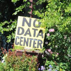 A yellow sign with black text reading “NO DATA CENTER” is nestled amid a planter of flowers in a garden in Kansas.  