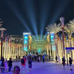 People walking around in a neon-lit outdoor walkway with palm trees at COP28