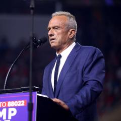 Robert F. Kennedy, Jr. stands at a podium speaking into a microphone. 
