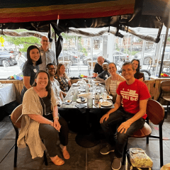 Switzer Fellows sit and stand around a restaurant table smiling. 