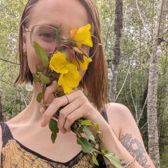 Laine holds yellow flowers in front of their face.