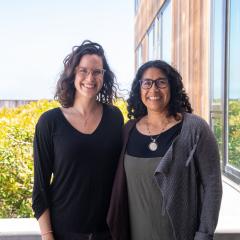 Melissa Cronin and Erika Zavaleta stand on a sunny balcony