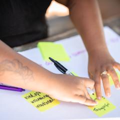 Hands place yellow post it notes with the words thoughtful, kind, intentional, on a white paper at a Switzer Fellows fall retreat.