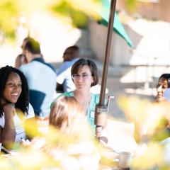 Seen through sunlit leaves, Switzer Fellows talking at outdoor picnic table
