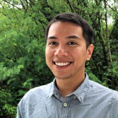 A photo of Aaron smiling against a background of lush green plants.