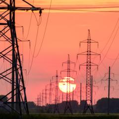 Power lines stretching into the distance with an orange sunset in the horizon.