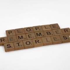 Scrabble tiles spell out "PEOPLE REMEMBER STORIES" on a white background