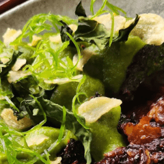 A close up of a meal created from all parts of a broccoli plant. It is bright green with a brown sauce on a white plate.