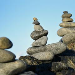 three pillars of stacked grey stones stand along a rock angling up from the bottom left to the middle right of the image. There is a blue sky in the background.