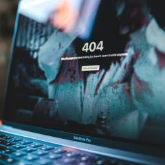 A 404 error shows on a Macbook laptop sitting on a desk at an angle. 