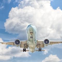 A silver airplane viewed from below against a blue sky and big white clouds.