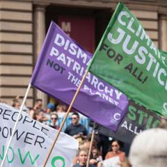 Colorful flags waving at a protest that read: climate justice for all! dismantle patriarchy not the planet, and People. Power. Now