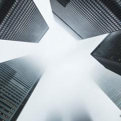 Looking up from the ground at a circle of five skyscrapers disappearing into clouds