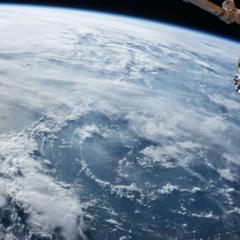 Picture of clouds over the ocean from space with a close-up of a satellite in the upper right corner.