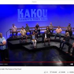 A screenshot of the youtube video showing KAKOU: Hawai'i's Town Hall on a blue background, a presenter standing to the left in a Hawaiian shirt, and a tiered stage with 16 people seated on a panel