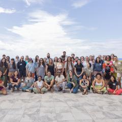 A group photo of the participants of the Fellowship to Friendship Switzer Network Celebration on a tile patio overlooking the ocean with white clouds and blue sky in the background.