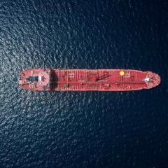 A large red ship is seen from far above, surrounded by dark blue/black water. 