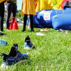 Shoes lying in green grass and kids standing outside a colorful bouncy house