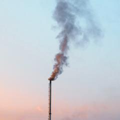 A think smokestack emits smoke into a pink and blue sky.