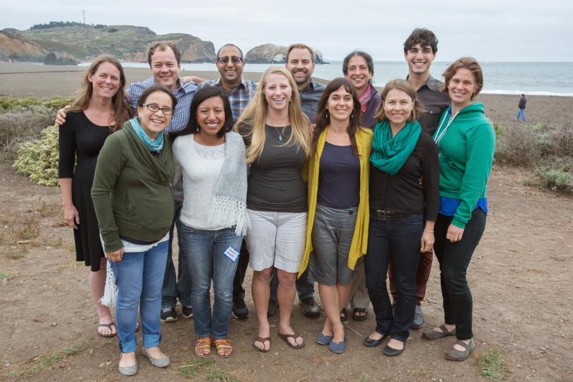 A group photo of twelve Switzer Fellows stand together smiling on a beach.