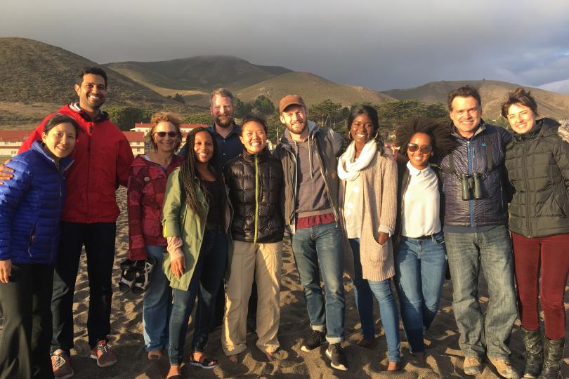 A group photo of Switzer Fellows standing together on the beach with hills and clouds in the background