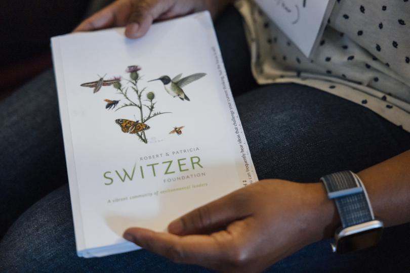 Hands hold a white notebook with an illustration and Switzer Foundation logo on it.