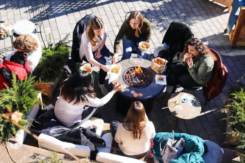 A group of people sit around a circular table on an outdoor patio, eating. 