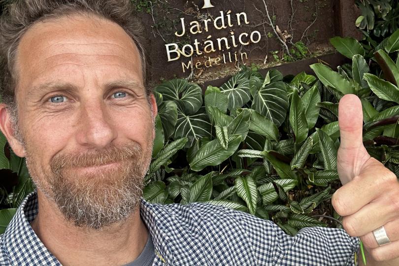 Dave Kramer takes a selfie giving a thumbs up in front of a sign for the Medelin botanical garden.