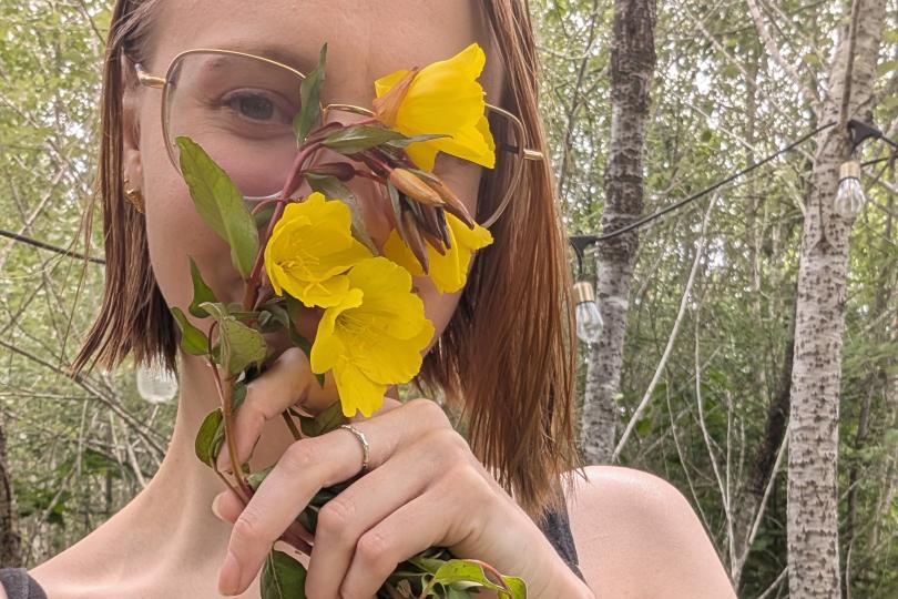 Laine holds yellow flowers in front of their face.