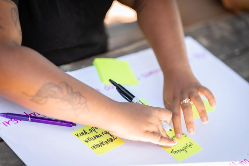 Hands place yellow post it notes with the words thoughtful, kind, intentional, on a white paper at a Switzer Fellows fall retreat.