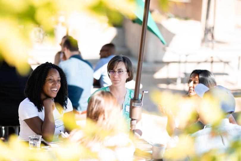 Seen through sunlit leaves, Switzer Fellows talking at outdoor picnic table