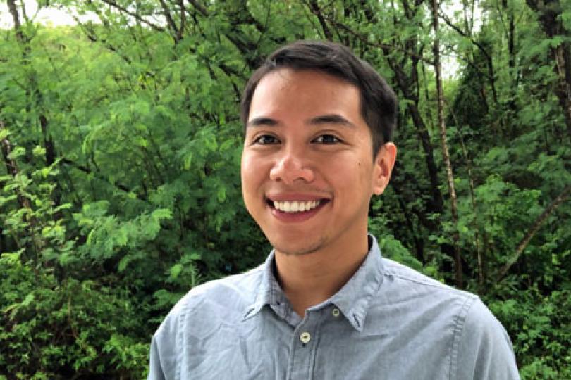 A photo of Aaron smiling against a background of lush green plants.