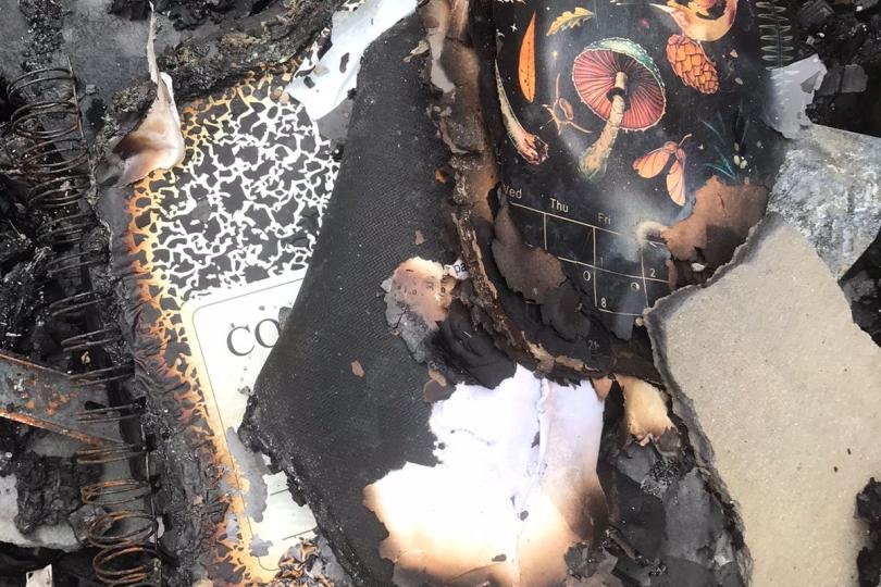 Burned composition notebooks and research papers sit in a pile of ashes from the fire.
