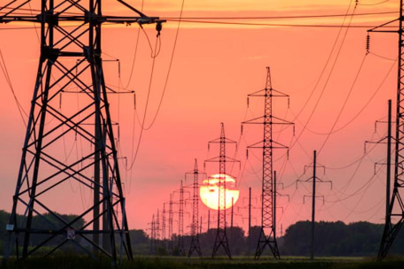 Power lines stretching into the distance with an orange sunset in the horizon.