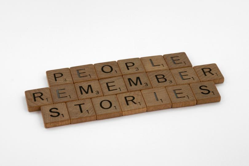 Scrabble tiles spell out "PEOPLE REMEMBER STORIES" on a white background