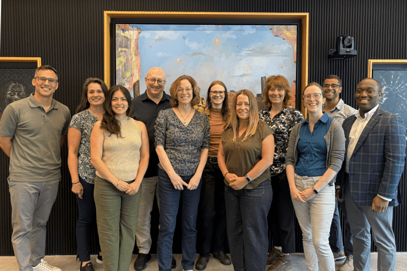 Switzer staff and board members smile for a group photo in front of a black wall with paintings on it.