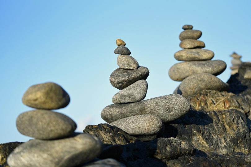 three pillars of stacked grey stones stand along a rock angling up from the bottom left to the middle right of the image. There is a blue sky in the background.