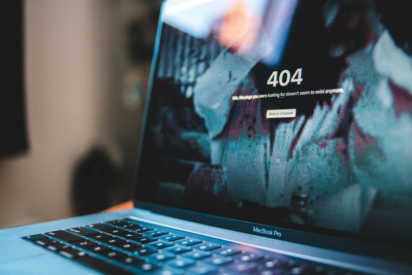 A 404 error shows on a Macbook laptop sitting on a desk at an angle. 