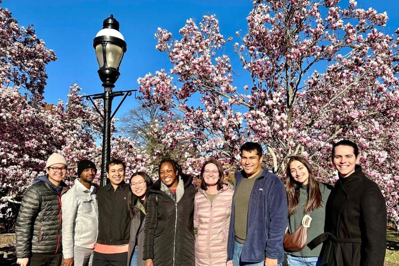 A group photo of Switzer Fellows standing in front of trees with pink cherry blossoms and a lamppost. 