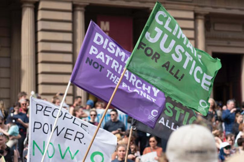 Colorful flags waving at a protest that read: climate justice for all! dismantle patriarchy not the planet, and People. Power. Now