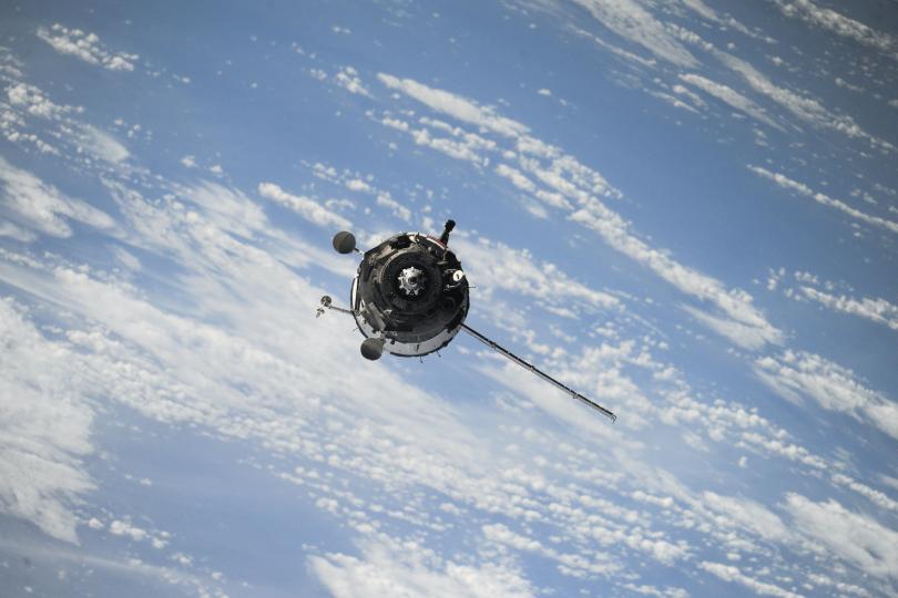 A satellite in orbit, seen from above against a backdrop of clouds and ocean on earth.