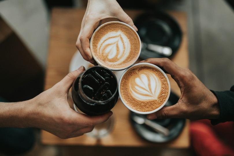 three beverages being cheers'ed together, two are lattes and one is a cold drink with ice.