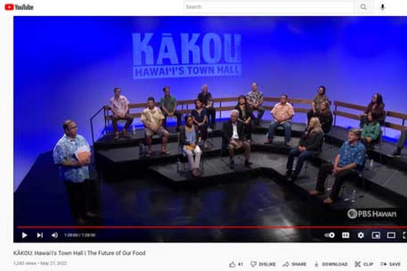 A screenshot of the youtube video showing KAKOU: Hawai'i's Town Hall on a blue background, a presenter standing to the left in a Hawaiian shirt, and a tiered stage with 16 people seated on a panel