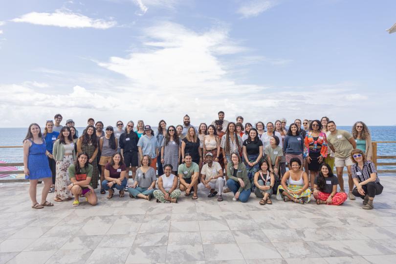 A group photo of the participants of the Fellowship to Friendship Switzer Network Celebration on a tile patio overlooking the ocean with white clouds and blue sky in the background.