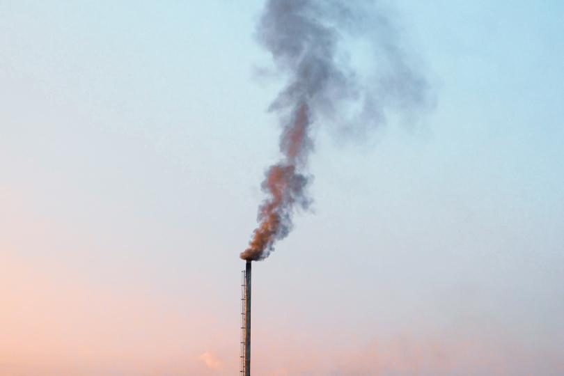 A think smokestack emits smoke into a pink and blue sky.